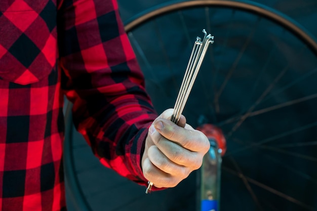 Taller profesional de bicicletas El mecánico sostiene radios en su mano sobre un fondo negro Un mecánico de bicicletas moderno y de moda con una camisa a cuadros roja sobre el fondo de una rueda