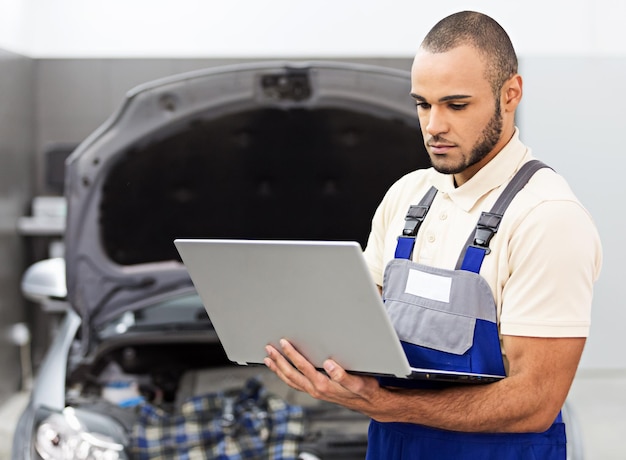 Taller de reparación de automóviles, mecánico masculino cerca del automóvil con computadora portátil