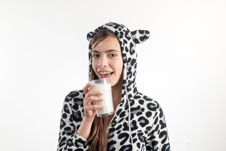 Foto talvez um banho quente e um copo de leite. jovem mulher bonita de pijama de vaca manchada segurando o copo de leite. adorável garota bebendo copo de leite. tomar um copo de leite morno antes de dormir