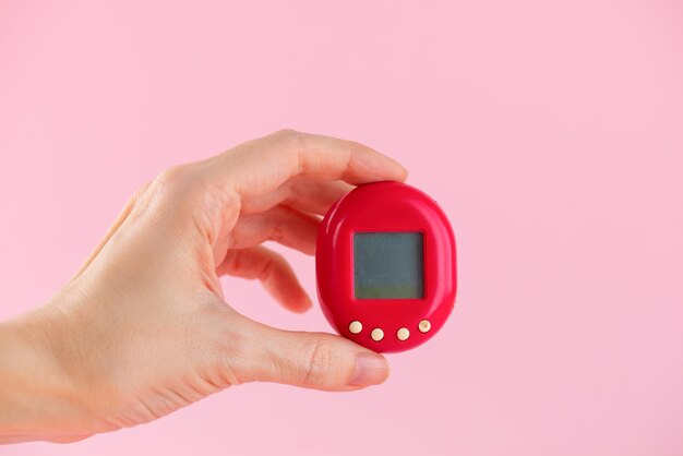 Foto tamagotchi-spielzeug in der hand auf einem rosa hintergrund beliebtes spiel, das sich in den 90ern um ein virtuelles haustier kümmert