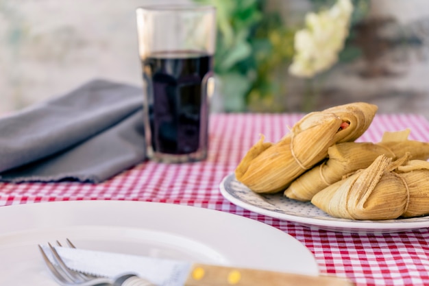 Tamales andinos tradicionais de milho e carne servidos em uma tábua de madeira em uma mesa de natureza morta com vinho