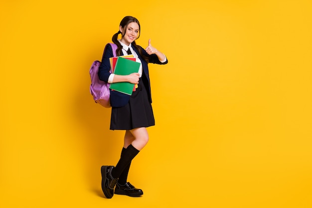 tamanho total do corpo de uma alegre colegial segurando um livro didático mostrando o polegar para cima