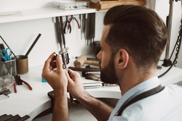 Tamaño exacto. Cerrar una foto de un anillo de medición de joven joyero con una herramienta en el taller. Concepto de fabricación de joyas. Taller de joyería. Manos del maestro