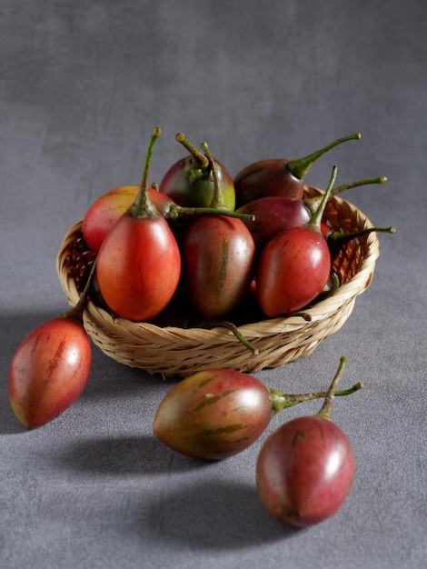 Tamarillo Frische reife Tamarillo in Korb und Sockel mit grauem Hintergrund Solanum Betaceum