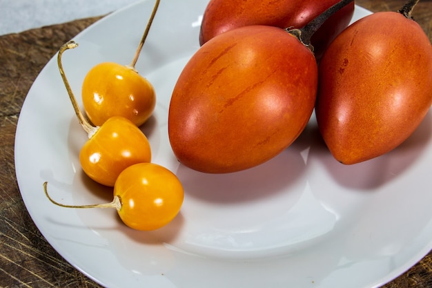 Tamarillo ou tomate árvore em uma placa de madeira ao lado de uvilla ou aguaymanto physalis