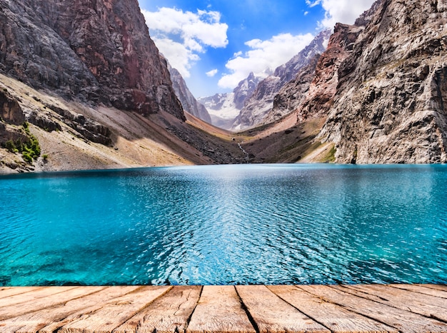 Foto tampo da mesa de madeira e lago de montanha com água azul-turquesa no sol na montanha rochosa
