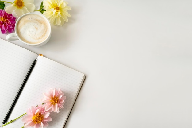 Tampo da mesa de um espaço de trabalho com lindas flores dahlia, xícara de café e um caderno, espaço de cópia.