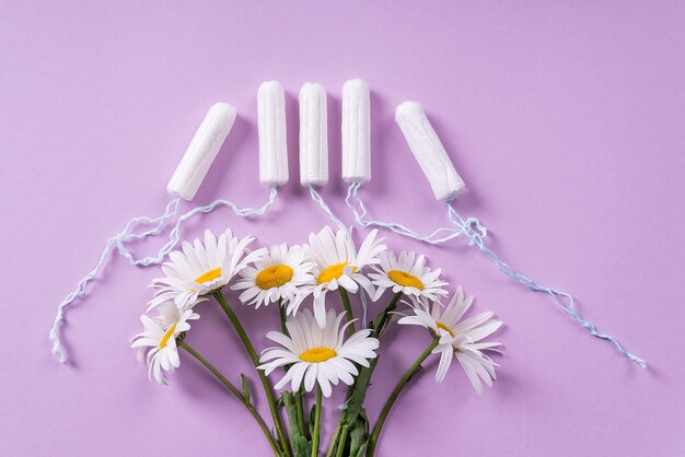 Tampões femininos e flores de camomila florescem em um plano de fundo lilás pastel