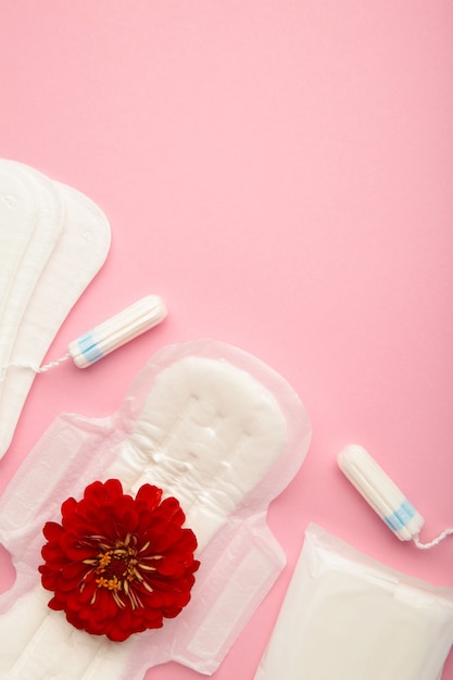 Tampões menstruais e absorventes em um fundo rosa. Ciclo de menstruação. Higiene e proteção. Uma rosa fica em uma almofada menstrual.