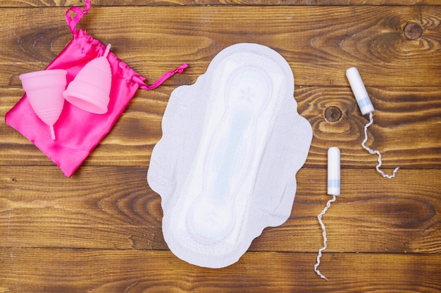 Tampones menstruales y copas menstruales sobre fondo de madera Vista superior Concepto de días críticos menstruación higiene femenina
