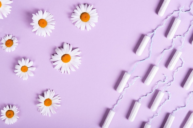 Los tampones de las mujeres y las flores de manzanilla florecen en un fondo lila pastel idea de salud de las mujeres