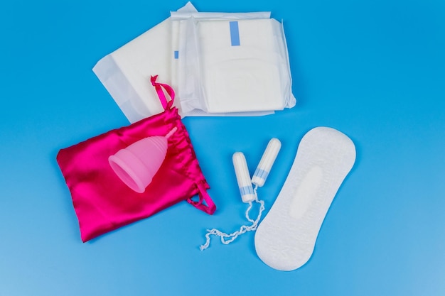 Tampones de toallas sanitarias y copa menstrual sobre fondo azul Vista superior Concepto de días críticos menstruación higiene femenina