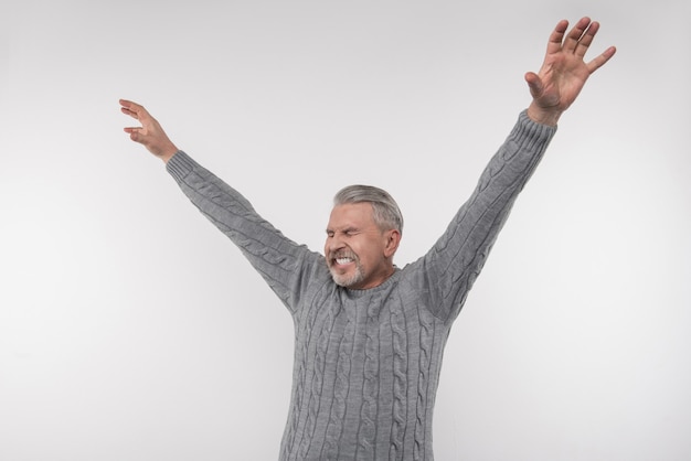 Tan feliz. Hombre emocional alegre sosteniendo sus manos mientras expresa su felicidad