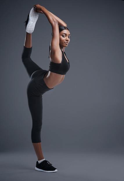 Tan feroz como flexible Retrato de estudio de una joven deportista que estira su cuerpo contra un fondo gris