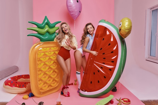 tan lindo. Longitud total de dos atractivas mujeres jóvenes en traje de baño jugando con adornos de frutas