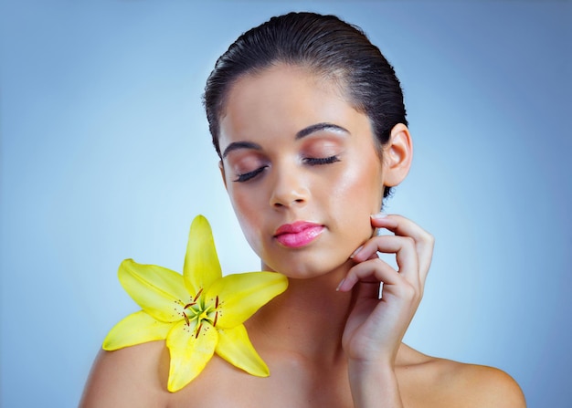 Tan natural tan hermosa Foto de estudio de una hermosa joven posando con una flor contra un fondo azul