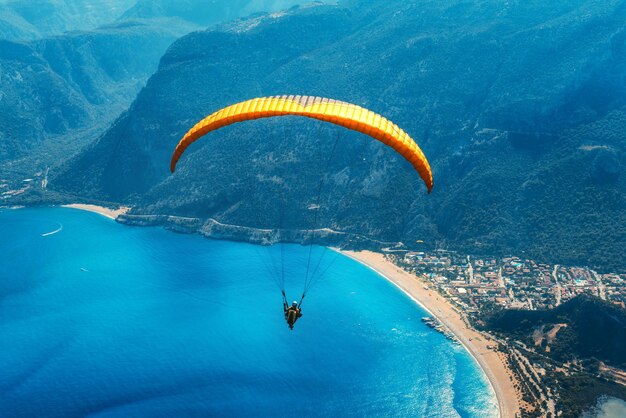 Tándem de parapente volando sobre el mar con agua azul y montañas