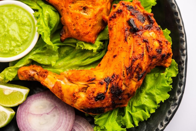 Tandoori Chicken ist ein Hühnchengericht, das durch Braten von in Joghurt und Gewürzen mariniertem Hühnchen in einem Tandoor- oder Lehmofen zubereitet wird, serviert mit Zwiebeln und grünem Chutney