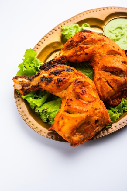 Tandoori Chicken ist ein Hühnchengericht, das durch Braten von in Joghurt und Gewürzen mariniertem Hühnchen in einem Tandoor- oder Lehmofen zubereitet wird, serviert mit Zwiebeln und grünem Chutney