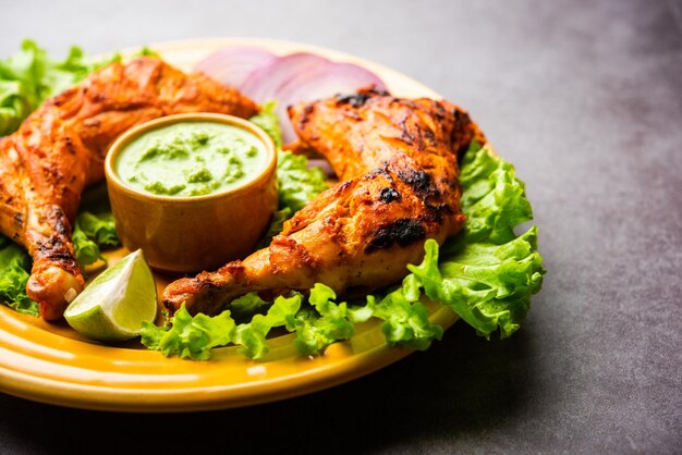 Tandoori Chicken ist ein Hühnchengericht, das durch Braten von in Joghurt und Gewürzen mariniertem Hühnchen in einem Tandoor- oder Lehmofen zubereitet wird, serviert mit Zwiebeln und grünem Chutney