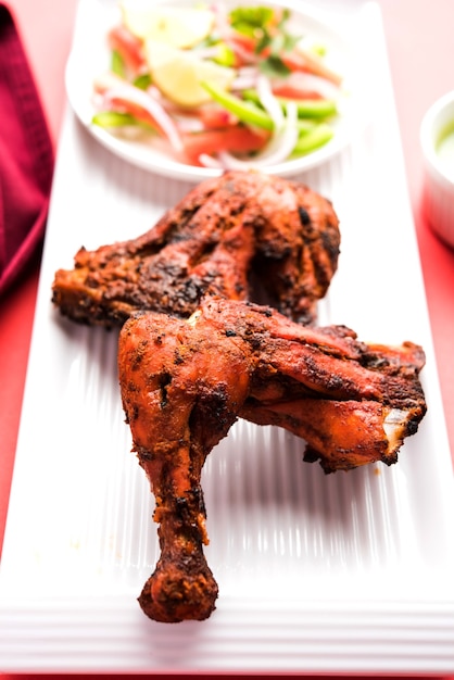 Tandoori-Huhn - zubereitet durch Braten von in Joghurt und Gewürzen mariniertem Hühnchen in einem Tandoor. Beinstücke im Teller serviert mit Salat & Chutney