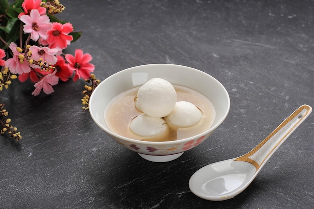 Tang Yuan (Wedang Ronde), chinesische Klebreis-Knödelbällchen mit Zucker-Ingwer-Sirup auf chinesischer Schüssel auf schwarzem Hintergrund für Wintersonnenwende-Neujahrsfest-Essen.