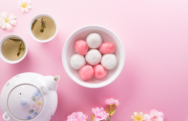 Tang Yuansweet Dumplings Balls eine traditionelle Küche für Midautumn Dongzhi Wintersonnenwende und chinesisches Neujahr mit Pflaumenblüte und Tee auf pastellfarbenem Hintergrund