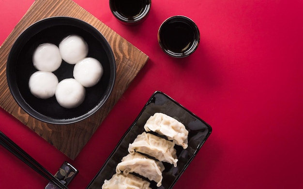 Tang Yuansweet Dumplings Balls eine traditionelle Küche für Midautumn Dongzhi Wintersonnenwende und chinesisches Neujahr mit Pflaumenblüte und Tee auf rotem Hintergrund