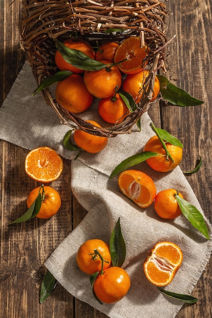 Tangerinas caindo da cesta. Laranjas, tangerinas, clementinas, frutas cítricas) com folhas verdes. Fundo de madeira, estilo rústico, vista de cima