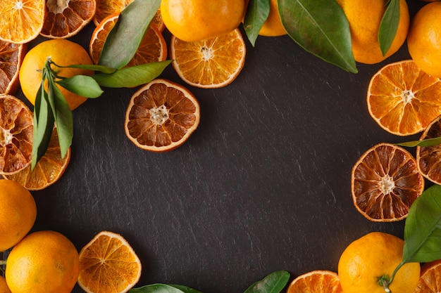 Tangerinas com folhas e laranja em fatias secas sobre a superfície de ardósia preta. Vista do topo