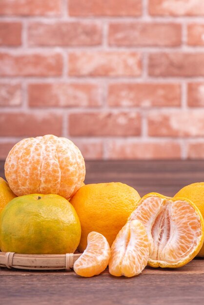 Tangerinas descascadas em uma cesta de peneira de bambu na mesa de madeira escura com fundo de parede de tijolo vermelho Conceito de design de frutas do ano novo lunar chinês close-up