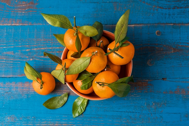 tangerinas frescas cruas com folhas na mesa de madeira azul.