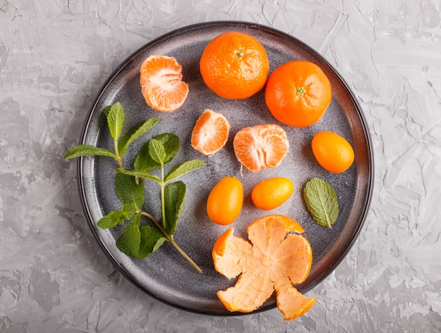 Tangerinas, kumquats e um ramo de hortelã na placa cerâmica em cinza