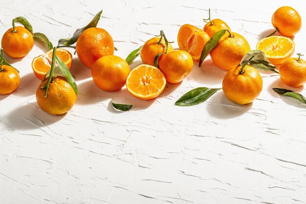 Tangerinas (laranjas, tangerinas, clementinas, frutas cítricas) com folhas verdes. Luz dura moderna, sombra escura. Fundo de massa branca, configuração plana criativa, espaço de cópia