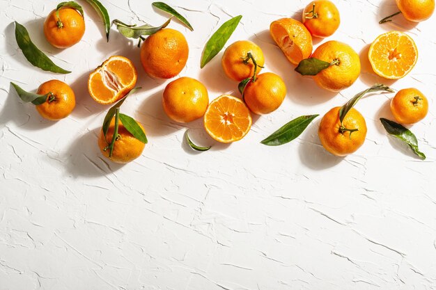 Tangerinas (laranjas, tangerinas, clementinas, frutas cítricas) com folhas verdes. Luz dura moderna, sombra escura. Fundo de massa branca, configuração plana criativa, vista superior