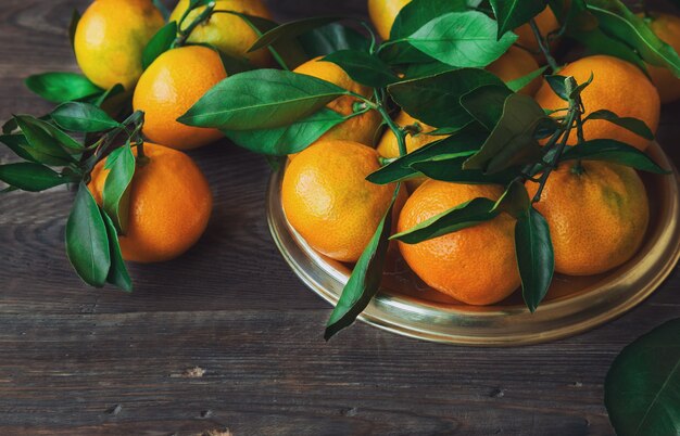 Tangerinas orgânicas frescas com folhas na superfície de madeira rústica.