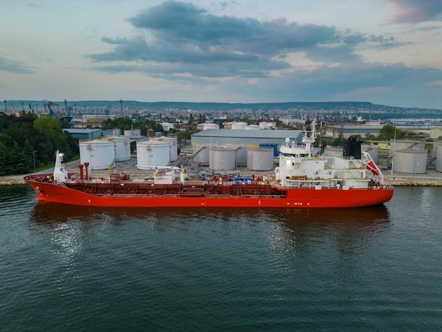 Tankschiff betankt an einem Ölterminal mit Lagersilos im Hafen, Luftaufnahme von einer fliegenden Drohne