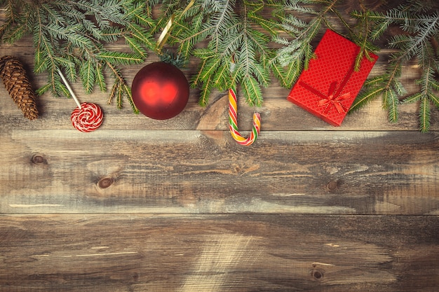 Tannenbaumaste mit Geschenkbox, Süßigkeiten, Kegel und Weihnachtsball auf hölzernem Hintergrund