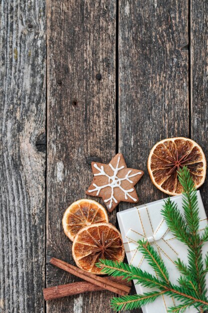 Foto tannenzweige, getrocknete orangen, geschenk, ingwerkeks, zimt auf holz.