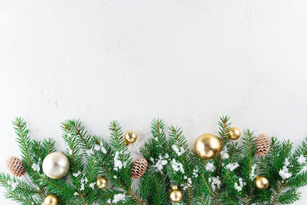 Tannenzweige mit goldenen Weihnachtskugeln und Zapfen auf hellem Hintergrund