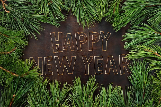 Tannenzweige mit langen Nadeln gegen eine dunkle Holzoberfläche Die Aufschrift Happy New Year