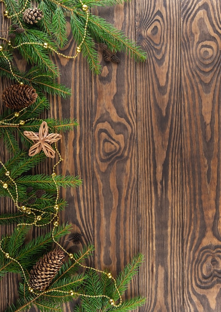 Tannenzweige verziert mit Tannenzapfen, einem Stern und einer Girlande auf braunem Holzhintergrund