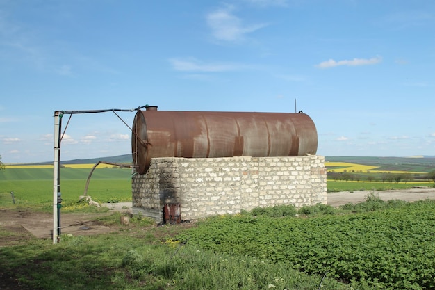 un tanque de agua oxidado en un campo con un fondo de cielo