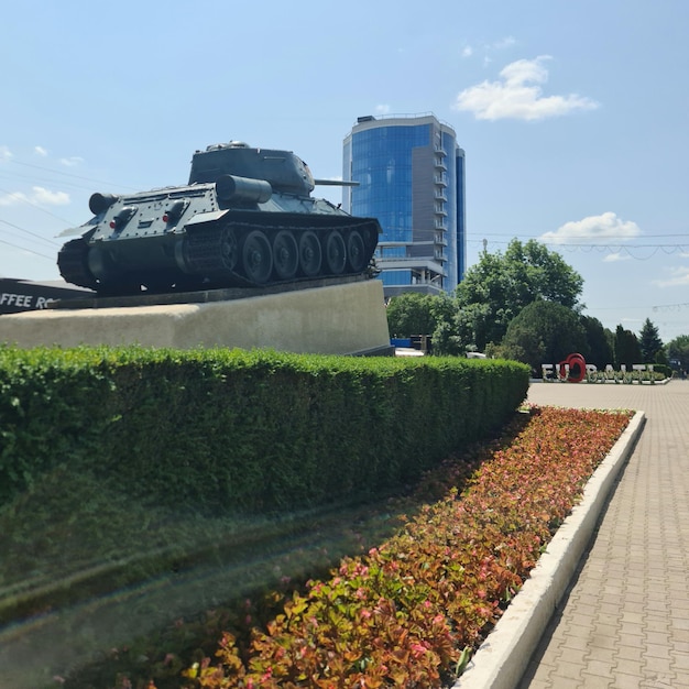 Un tanque grande está en exhibición frente a un edificio con un cielo azul de fondo.