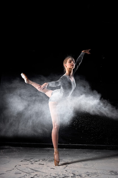 Tanzen im Mehlkonzept. Kaukasische Ballerina-Tänzerin im Staubnebel. Porträt einer Tänzerin in Mehl auf schwarzem, isoliertem Hintergrund, die sich anmutig bewegt. Menschen, Kunst, Tanzkonzept