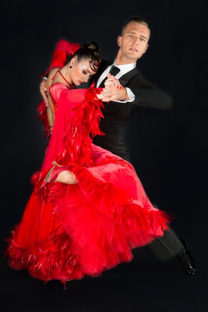Tanzen Sie Ballsaalpaare in der roten Kleidertanzhaltung lokalisiert auf schwarzem Hintergrund. sinnliche Profitänzer tanzen Walzer, Tango, Slowfox und Quickstep.
