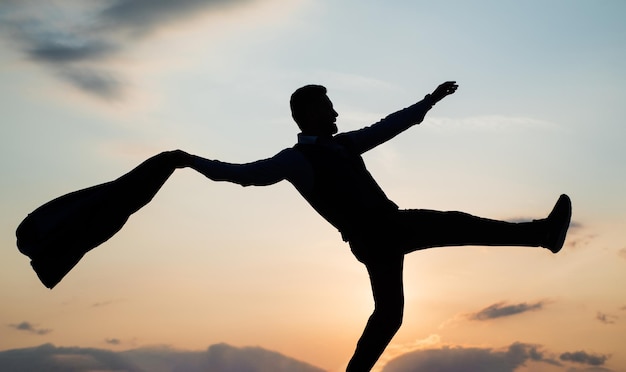 Tanzende Mannsilhouette mit Jacke gegen Sonnenunterganghimmel, Freiheit.