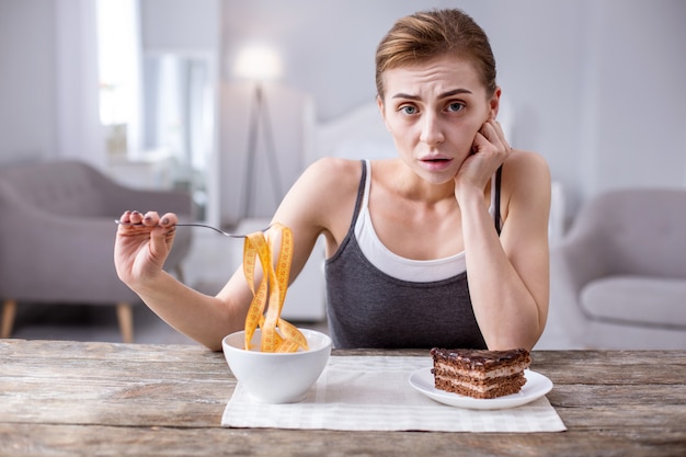 Tão faminto. jovem deprimida sentada à mesa enquanto faz dieta