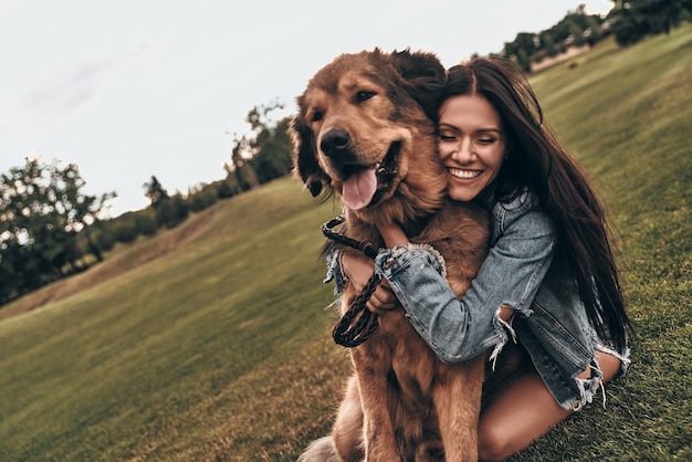 Foto tão fofo e adorável. mulher jovem e bonita mantendo os olhos fechados e sorrindo enquanto abraça o cachorro ao ar livre