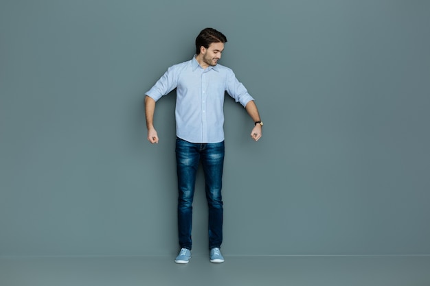 Tão pesado. Homem alegre e simpático positivo sorrindo e olhando para as mãos enquanto cuida das malas